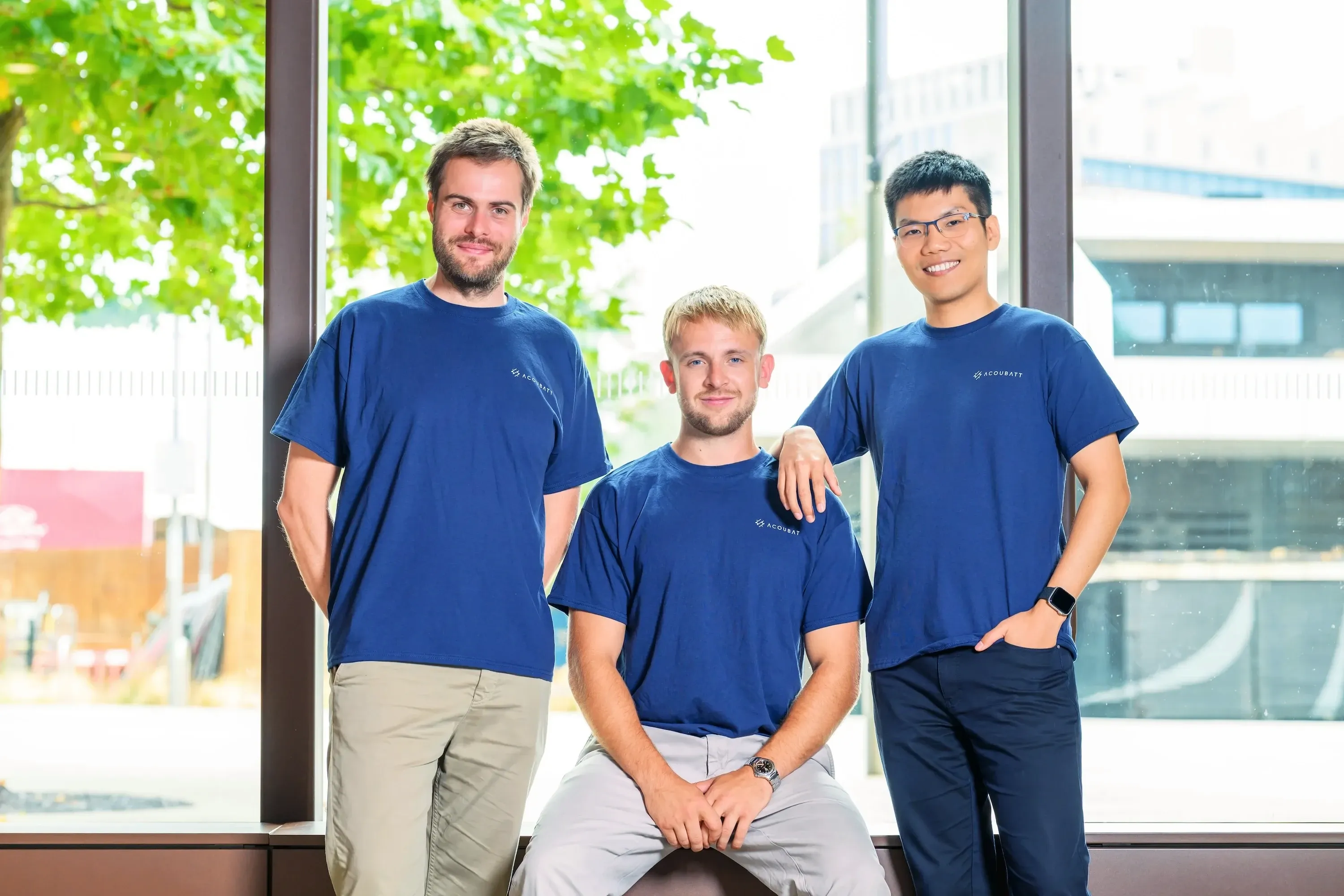 Lukas Noll, Arthur Fordham and Chris Xu, the AcouBatt team, in AcouBatt T-shirts in front of a window.